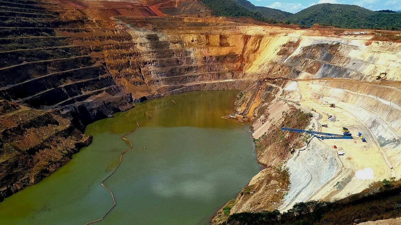 Terraced open-pit mine with a pit lake, surrounded by green hills